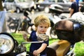 Small kid sits on motorbike and smiles. Sincere emotions from little boy. Motorbikes on street background. Street full