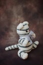 a small knitted white with black stripes kitten with a long thin tail and a white butterfly on its neck sits Royalty Free Stock Photo