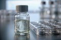 Small laboratory glass vial filled with clear liquid and a plastic multi-well plate on reflective surface in a modern research Royalty Free Stock Photo