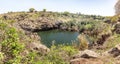 A small lake with fish framed by hexagonal rocks with overgrown bushes and trees on the banks in Yehudia National Natural Park in