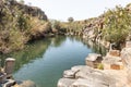 A small lake with fish framed by hexagonal rocks with overgrown bushes and trees on the banks in Yehudia National Natural Park in