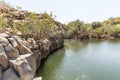 A small lake with fish framed by hexagonal rocks with overgrown bushes and trees on the banks in Yehudia National Natural Park in