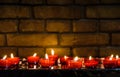 Small lighted candles in red glass holders in front of a brick wall