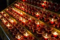 Small, lighted votive candles in red glass candlesticks, lined up on a candle holder stand Royalty Free Stock Photo