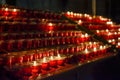 Small, lighted votive candles in red glass candlesticks, lined up on a candle holder stand