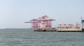 A small lighthouse is located on the breakwater and Large cargo cranes stand on a pier in the Mediterranean port of Haifa in