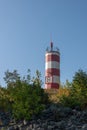 A small lighthouse stands on a cape among trees and bushes