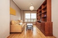 Small living room furnished with a reddish-colored wooden bookcase, a mustard-colored three-seater sofa, and a window with views