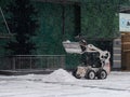 A small loader with a bucket removes snow from a road on a city street