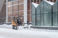 A small loader excavator clears snow from the road along the glass walls