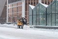 A small loader excavator clears snow from the road along the glass walls