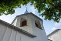 Small and low bell tower near the church with bricks, painted white, with an Orthodox Christian cross on top on blue sky backgroun Royalty Free Stock Photo