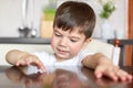 Small male preschooler has curious look at kitchen table, waits for brealfast, has appealing appearance, dressed in casual t shirt