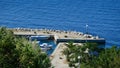 Small marina molo pier in shape of an arc with some fishing boats and palms on the shore.