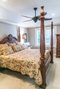 Small Master bedroom with a large four poster wood bed and an old fashioned floral comforter with a window. Royalty Free Stock Photo