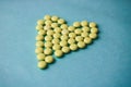 Small medical pharmaceptic round yellow pills, vitamins, drugs, antibiotics in the form of a heart on a blue background, texture. Royalty Free Stock Photo