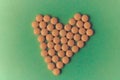 Small medical pharmaceptic round yellow pills, vitamins, drugs, antibiotics in the form of a heart on a green background, texture. Royalty Free Stock Photo