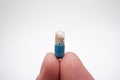 Small medicine medicament capsule half blue half transparent held between fingers. Close up studio macro shot, isolated on white Royalty Free Stock Photo