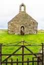 Small medieval Welsh Chapel in field, Anglesey. Gate in foreground