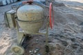 Small metal concrete mixer on wheels with rounded body, electric drive and red wheel of tipping cement mortar on jagged rim