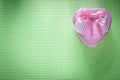 Small metal pink heart-shaped present box on green background ho