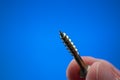 Small metal threaded screw held by Caucasian male hand between fingers. Close up studio macro shot,  on blue background Royalty Free Stock Photo