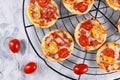 Small mini pizzas topped with cheese, tomato, yellow and red bell peppers and salami sausage on round black grid Royalty Free Stock Photo