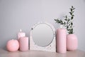 Small mirror, burning candles and vase on table near light wall Royalty Free Stock Photo