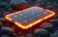 Small mobile solar panel glows orange. Renewable energy source on stones. Portable modern solar tech, eco-friendly electricity Royalty Free Stock Photo