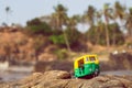 Small model of auto rickshaw vehicle moves across a palm trees beach in India.