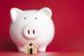 Small model house in front of a white piggy bank on a red background. Royalty Free Stock Photo