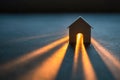 Small model house illuminated from inside casting glowing beams of light through an arched doorway on a dark textured surface with Royalty Free Stock Photo
