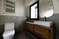 Small modern design bathroom with gray stone effect tiles, mirror on the wall, white porcelain sink cantilevered on wooden cabinet Royalty Free Stock Photo