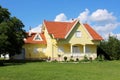 Small modern yellow suburban family house with garage surrounded with green grass and trees