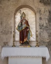 Small monument to a Bishop of Granada with a colorful statue and two candelabaras outside in a neighborhood of Granada, Spain.