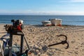 Small motor winch and anchors and small wooden fishing rowboats on a sandy beach