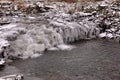 A small mountain river flows down in a frozen cascade into a valley with rocky ridges, powdered with the first snow Royalty Free Stock Photo