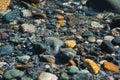 Small multicolored stones on the bank of a mountain stream with crystal clear glacial water. Top view. Royalty Free Stock Photo