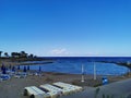 A small municipal beach in the bay of the Mediterranean Sea with sun loungers and closed parasols against the blue sky