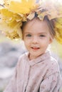 Small mysteriously smiling girl in a wreath of yellow leaves. Portrait