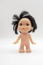 A small naked doll with black hair stands on a white background