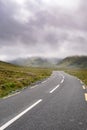 Small narrow asphalt road into mountains. Connemara area, county Galway, Ireland. Low cloudy sky over mountains. Vast fields on Royalty Free Stock Photo