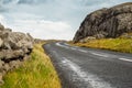 Small narrow asphalt road between traditional stone fence and rock . Burren area, West coast of Ireland. Warm sunny day. Cloudy Royalty Free Stock Photo