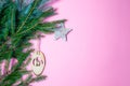 A small nativity scene carved out of wood hangs from a spruce branch in front of a matte pink background. christmas invitation. Royalty Free Stock Photo