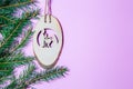 A small nativity scene carved out of wood hangs from a spruce branch in front of a matte pink background. christmas invitation Royalty Free Stock Photo