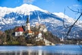 Small natural island in the middle of alpine lake with church dedicated to assumption of Mary and castle with snowy mountains