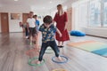 Small nursery school children with female teacher on floor indoors in classroom, doing exercise. Jumping over hula hoop Royalty Free Stock Photo