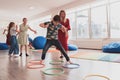 Small nursery school children with female teacher on floor indoors in classroom, doing exercise. Jumping over hula hoop Royalty Free Stock Photo