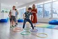 Small nursery school children with female teacher on floor indoors in classroom, doing exercise. Jumping over hula hoop Royalty Free Stock Photo