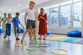 Small nursery school children with female teacher on floor indoors in classroom, doing exercise. Jumping over hula hoop Royalty Free Stock Photo